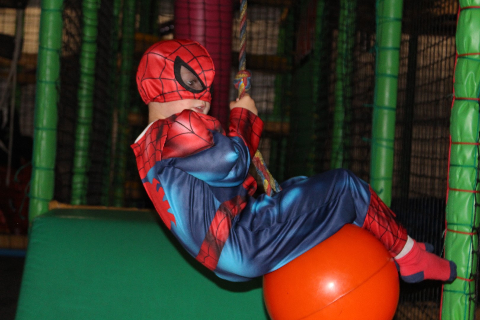 Boy in a Spider-Man costume swinging on a rope swing in the soft play frame