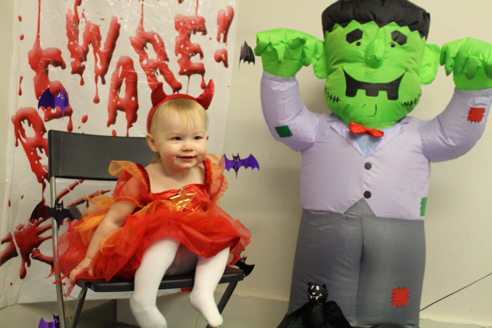 Toddler in a red devil costume next to an inflatable Frankenstein at a FuZe Halloween event