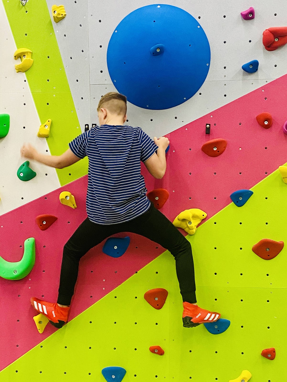Boy in a striped T-shirt climbing the pink and lime FuZe climbing wall