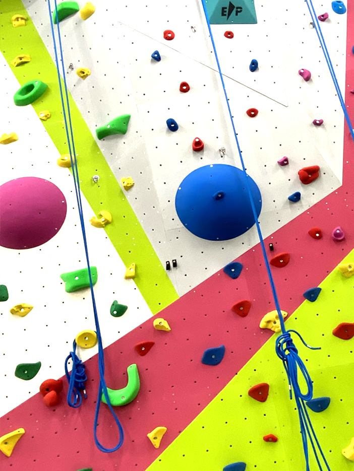 The FuZe climbing wall in bright pink, lime and white, dotted with colourful holds, with blue safety ropes hanging down